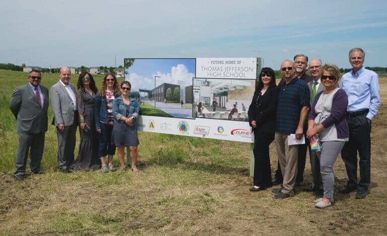 Ellie Standing with others in front of a sign announcing additional schools for the Sioux Falls, SD school district.